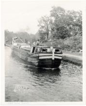 Canal boat travel down river; man and boat steering boat