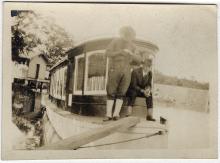 Parked passenger boat in river; 2 men at front of the boat