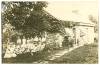 Group of children sitting in countryside outside of a stone home listening to librarian read a story