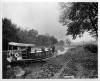 House boat in canal, windows with curtains and cover on front; 2 men at back of boat 