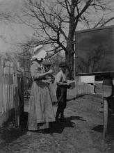 Woman in bonnet with 2 children standing outside of book wagon, reading books