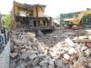 Bulldozers knock down building with brick rumble in foreground