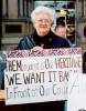 Photo of Mary Miltenberger holding a sign "The Monument is Our Heritage We Want it Back in Front of Our Courthouse"